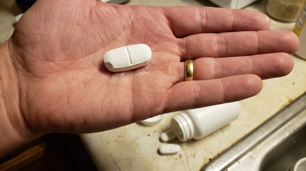 A large chalky magnesium tablet in the palm of a hand over a kitchen sink